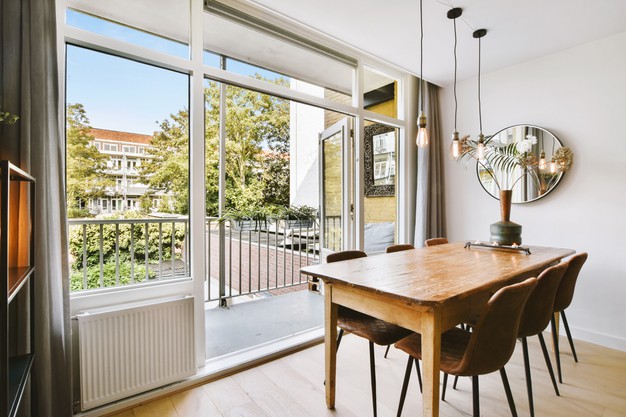 wooden-table-with-vase-and-chairs-placed-near-opened-balcony-door-in-light-dining-room-at-home_305343-110